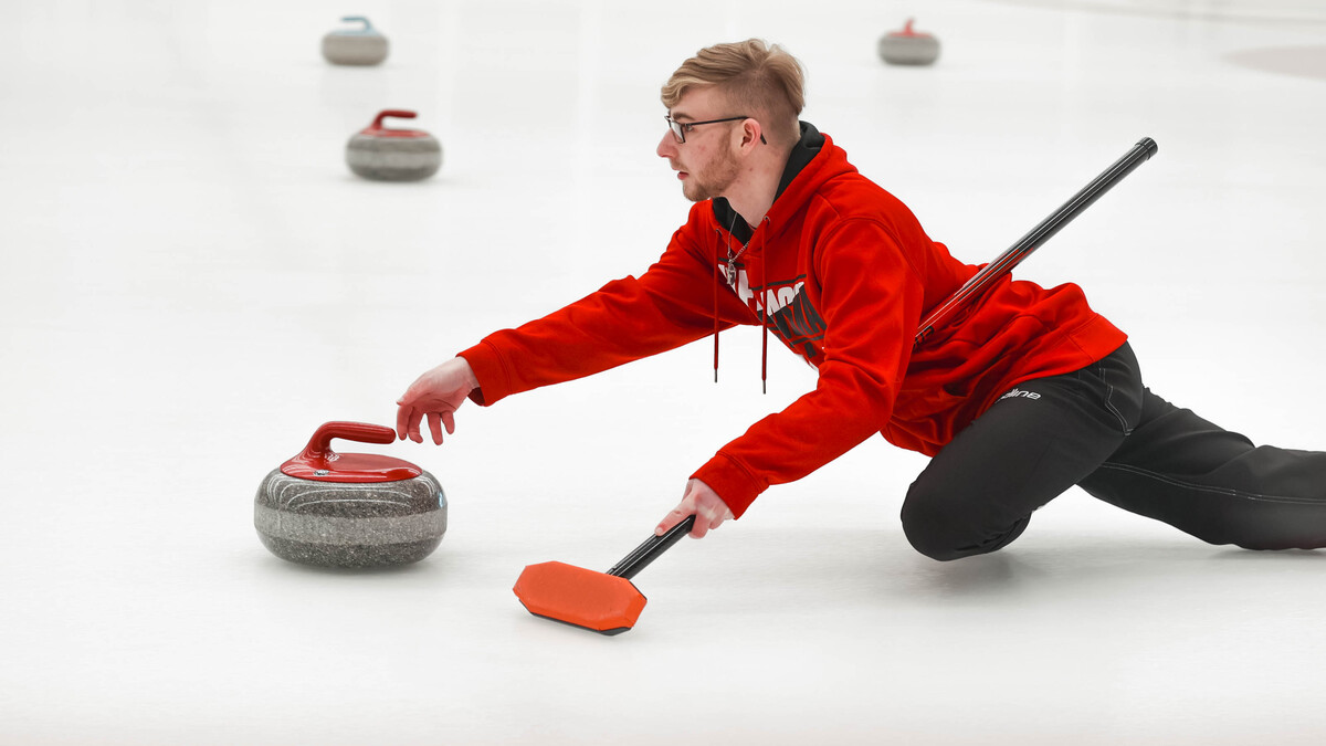 Brett Johnson slides a curling stone Saturday during the club team's bonspiel at the Breslow Hockey Center.
